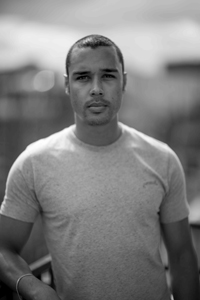 Black and white portrait of a man wearing a light-colored t-shirt looking directly at the camera.