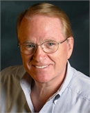 A smiling man with light hair and glasses wearing a light blue button-down shirt.