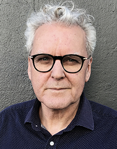 A man with wavy gray hair and black-rimmed glasses looking directly at the camera.
