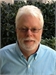 A man with white hair, a white beard, and glasses wearing a light blue button-down shirt.