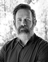 Black and white portrait of a man with a full beard and dark hair looking toward the camera.