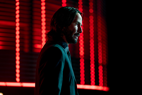 Profile of a man with dark hair and a beard looking right against a background of vertical red lights.