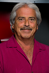 A smiling man with gray hair and a mustache wearing a magenta button-down shirt.