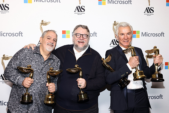Three men smiling and holding gold trophies in front of a white backdrop with logos.