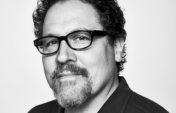 Black and white headshot of a man with curly hair, glasses, and a salt-and-pepper goatee.