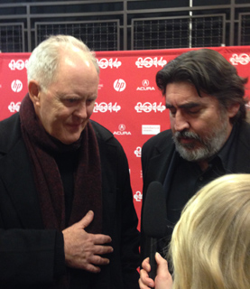 Two men with microphones in front of a red backdrop with "2014" logos.