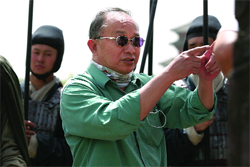 A man in a green shirt and sunglasses points forward while standing near people in dark headgear.