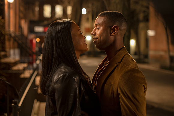 A man and woman face each other closely and smile on a city street at night.