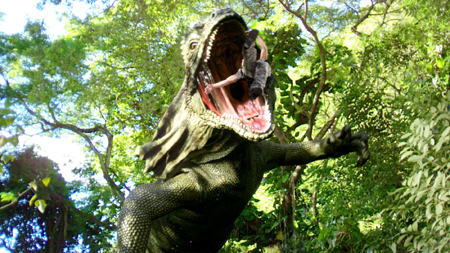 A large green dinosaur statue with an open mouth stands amidst lush green trees.