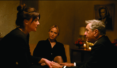 A woman in profile, a woman facing forward, and an older man sitting together in a warm, low-lit room.