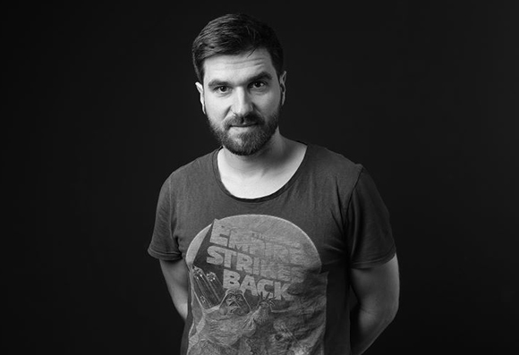 A bearded man wearing a Star Wars: The Empire Strikes Back t-shirt, looking at the camera against a black backdrop.