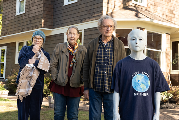 An elderly woman, a middle-aged woman, an elderly man, and a grey alien standing in front of a house.