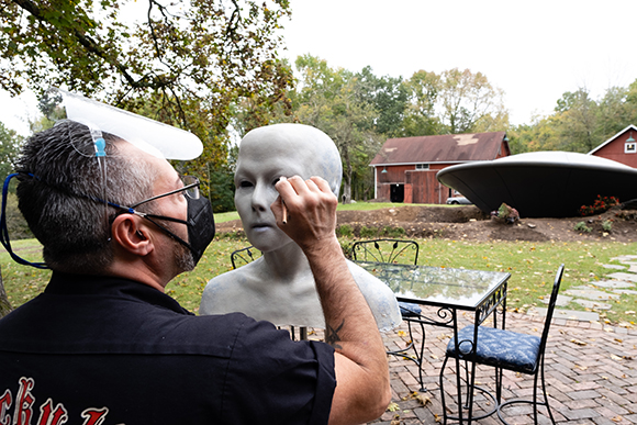 A man in a black shirt uses a tool to refine a white mannequin head outdoors.