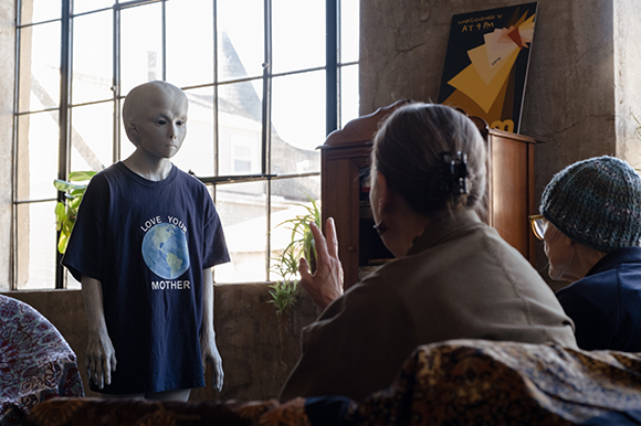 A person in a black t-shirt with a blue circular graphic stands near a person seen from behind.