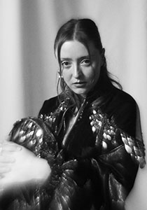 A woman with long hair looks toward the camera wearing a dark, sequined top.