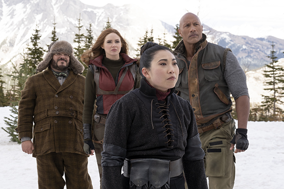 Four people in outdoor gear stand together in a snowy, mountainous landscape.