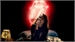 A person singing into a microphone against a dark background with a bright red glowing shape behind them.