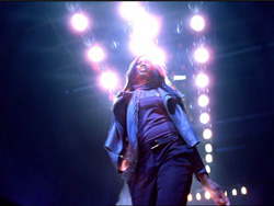 A person singing on stage under bright, glowing spotlights.