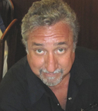 A man with wavy gray hair and a gray goatee wearing a black shirt.