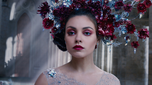 A woman with dark hair and pink eye makeup wearing a large, ornate headpiece of red flowers and silver accents.