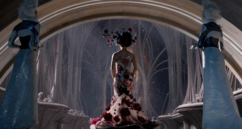 A woman in a red and white floral gown stands centered before a large archway looking out at a white forest.
