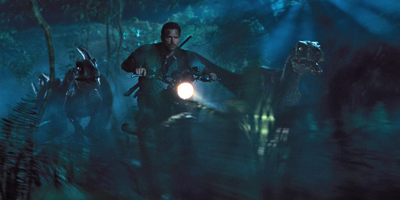 A man runs through a dark, misty jungle at night, flanked by two large dinosaurs.
