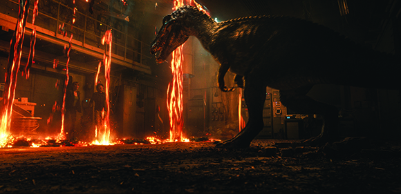 A large dinosaur stands in a dark warehouse as glowing streams of molten lava fall around it.