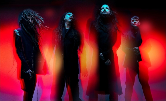 Four long-haired musicians in dark clothing stand against a glowing red and black background.