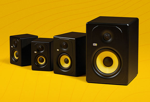 Four black KRK studio monitors of different sizes lined up on a yellow background.