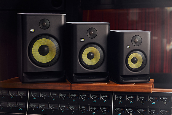 Three black KRK studio monitors with yellow woofers arranged by size on a professional mixing desk.