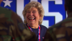 A blonde woman laughs while wearing a USA lanyard, flanked by two people in camouflage uniforms.