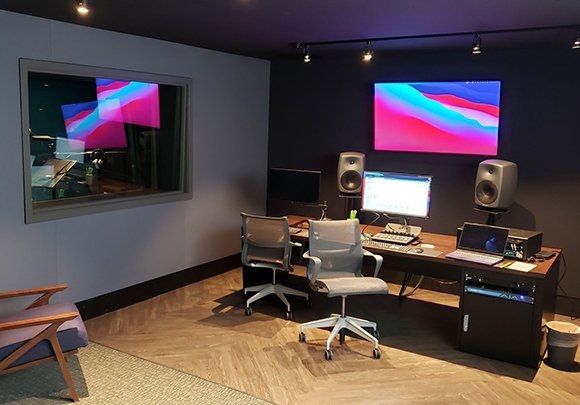 A recording studio control room with a large desk, computer monitors, studio monitors, and office chairs.