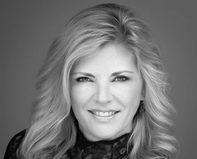 A smiling woman with long, wavy blonde hair looking directly at the camera in a black and white portrait.