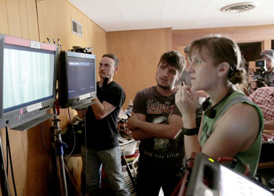 Three crew members look intently at video monitors in a production setting.