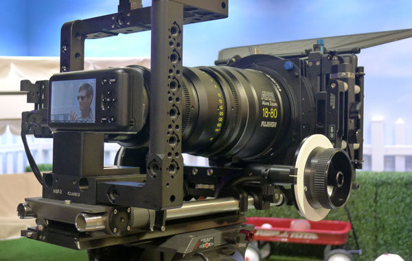 Close-up of a professional cinema camera rig with a large Fujinon zoom lens and a monitor displaying a man.