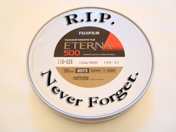A round metal film canister with "R.I.P., Never Forget." printed on the lid. The canister contains Fujifilm ETERNA 500 film.