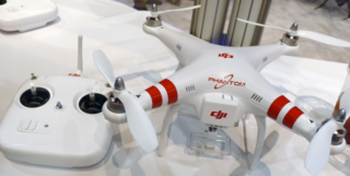 A white DJI Phantom drone with red stripes on its arms sits next to its white remote control on a table.