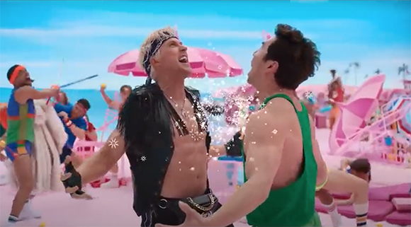 Two men in colorful tank tops dance on a beach with pink sand and pink umbrellas.