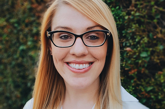 A smiling woman with blonde hair and black-rimmed glasses looking at the camera.