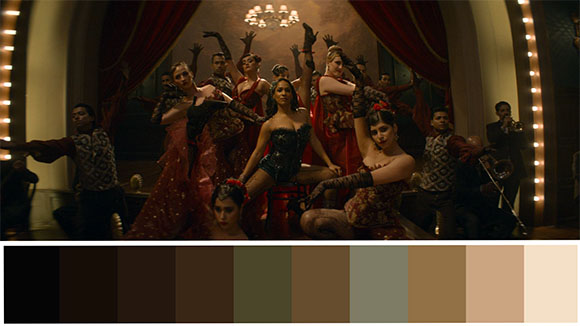 Performers in red and black costumes pose in a grand, dimly lit room with red curtains and warm lighting.