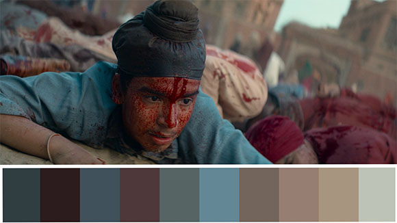 A person with blood on their face and blue shirt lies on the ground in a dusty setting.