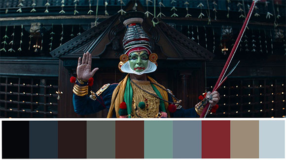 A Kathakali performer with green face paint, elaborate headgear, and colorful attire holding a staff.