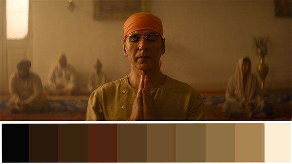 A man in an orange headwrap sits with eyes closed and hands in prayer position.
