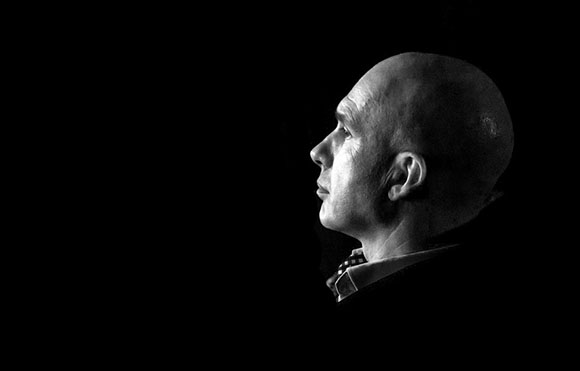 Black and white profile of a bald man looking up against a dark background.