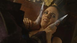 A woman grimaces as two large, sharp claws press against her neck and face.