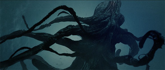 A dark, massive creature with many long, thick tentacles swimming in deep blue water.