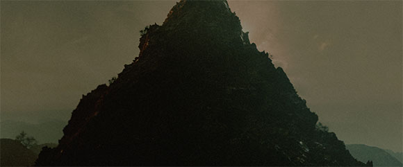 Silhouette of a dark, craggy mountain peak against a hazy, overcast sky.