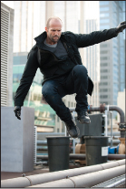 A man in dark clothing leaps through the air above rooftop pipes and equipment.