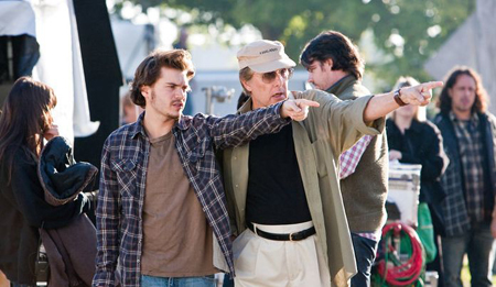 Two men stand outdoors, both pointing their fingers toward something off-camera.
