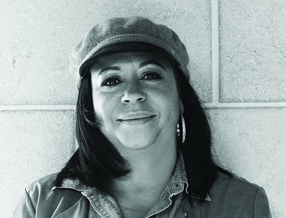 Black and white close-up portrait of a smiling woman wearing a newsboy cap and hoop earrings.